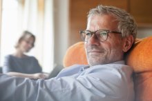 An older man sitting in a chair, looking pensive