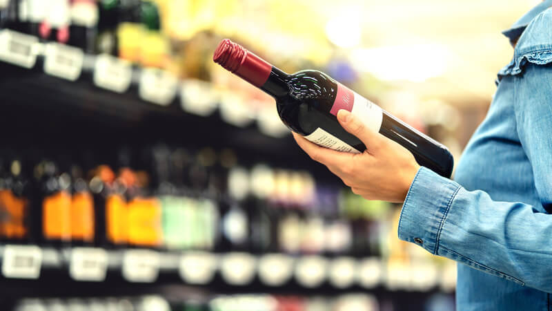 Hands holding a bottle of alcohol in a liquor store setting.