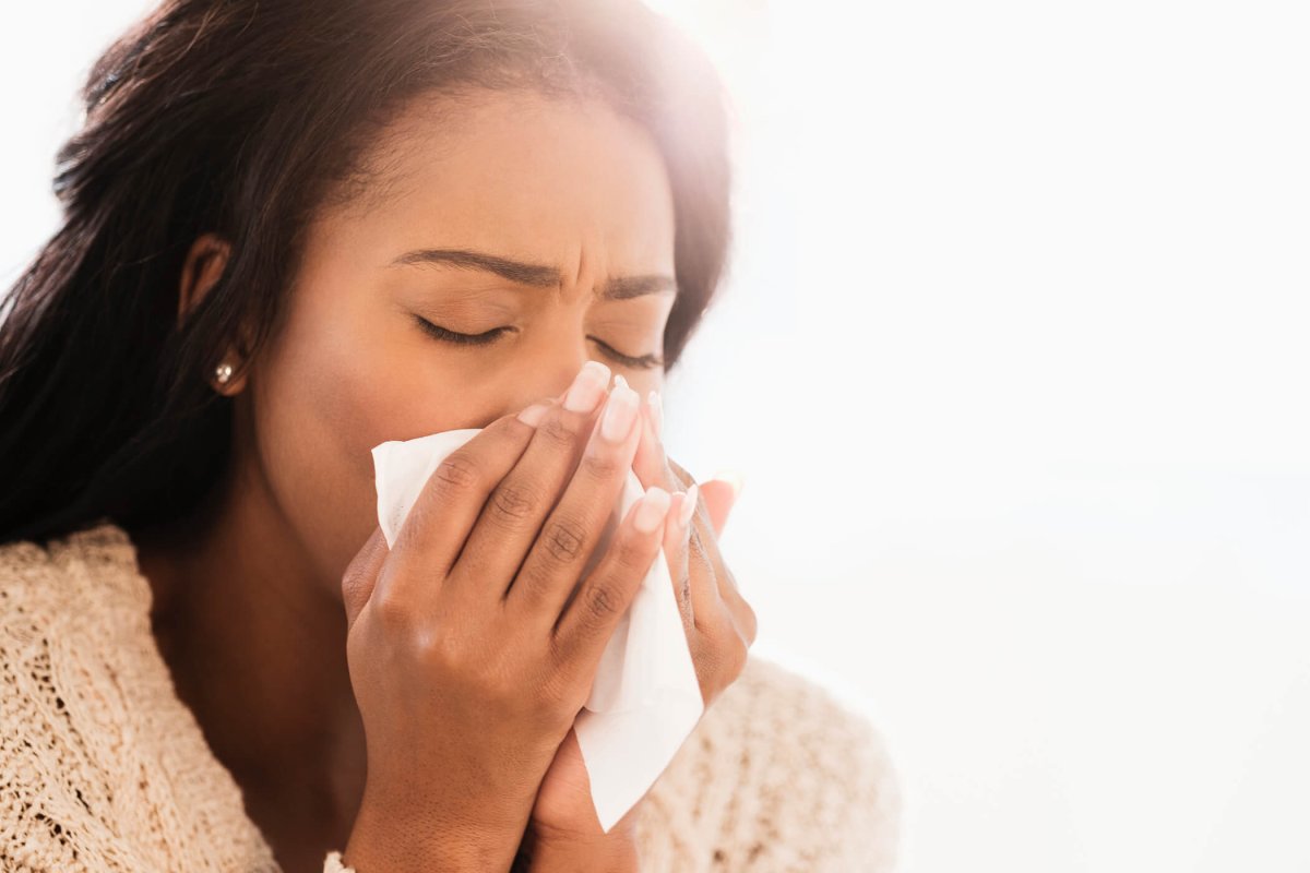 Woman in white sweater using tissue to blow her nose.